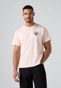 Svijetlo ružičasta pamučna majica kratkih rukava. Ima mali, šareni vezeni dizajn i crnu oznaku "Levi's" na prsima.