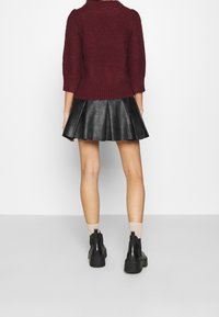 Burgundské svetr s krátkými rukávy a žebrovaným lemem, kombinovaný s černou plisovanou koženou sukní. Černé kotníkové boty dokončují tento outfit.