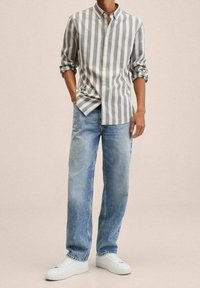 Camicia a righe verde chiaro e bianca, abbinata a jeans azzurri e sneakers bianche. Vestibilità casual, maniche arrotolate e design rilassato.