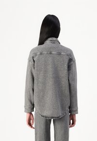Veste en denim gris au fit décontracté, avec des embellissements subtils et un ourlet arrondi. Manches longues avec détails aux poignets.