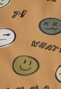 Bomuldsstof i tan med tegneserieansigtudtryk i grøn, hvid og sort. Teksten inkluderer "HVA?" og forskellige emojis i legende designs.