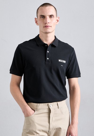 Juodas medvilnės polo marškinėliai trumpomis rankovėmis ir dviem mygtukais. Kairėje krūtinės pusėje yra baltas "Moschino" logotipas.