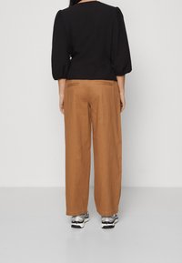 Top alto a maniche puff nere abbinato a pantaloni ampi beige. I pantaloni hanno tasche posteriori; le scarpe sono di stile atletico grigio e nero.