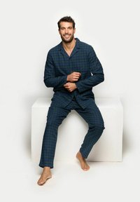 Męski komplet piżam w niebieską kratę, składający się z koszuli na guziki oraz dopasowanych spodni. Miękka tkanina o luźnym kroju, prezentująca się na białym stosie.