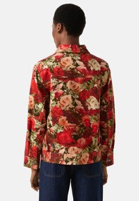 Czerwona jeansowa kurtka w kwiaty z dużymi wzorami róż, z ostrym kołnierzem i zapięciem na guziki oraz dwoma bocznymi kieszeniami, prezentowana od tyłu.