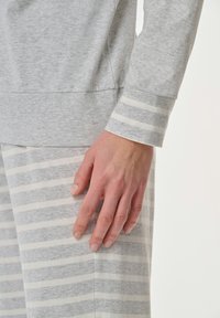 Grå loungewear-set bestående av en långärmad topp med enfärgade grå manschetter och byxor med vita ränder. Mjuk, texturerad tyg med en avslappnad passform.