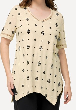 Beige top met zwarte geometrische patronen, met een V-hals en korte mouwen. Zachte stof met zijsplitten en gestructureerde rand bij de halslijn.