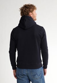 Sudadera azul marino con un bolsillo tipo canguro y capucha ajustable con cordón, hecha de material suave. Puños y dobladillo de canalé para un ajuste ceñido.