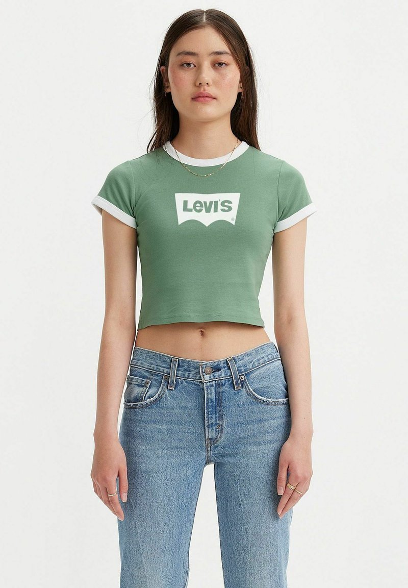 T-shirt verde corto con colletto e polsini bianchi, caratterizzato da un prominente logo bianco Levi's sulla parte anteriore. Indossato con jeans azzurri chiari.