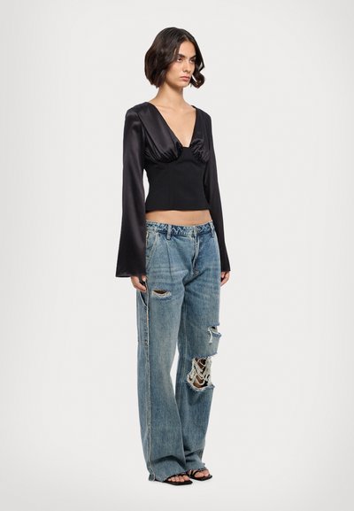 Black satin long-sleeve top with a deep V-neck and ruched detail, paired with light blue distressed wide-leg jeans featuring frayed patches.
