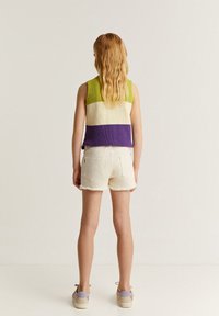 Top de punto sin mangas en verde, blanco y púrpura; combinado con pantalones cortos desgastados de color beige claro y zapatillas beige con acentos púrpuras.