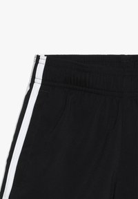 Shorts deportivos negros con una cintura elástica, bolsillos laterales y dos rayas blancas verticales a lo largo de los lados. Textura suave.