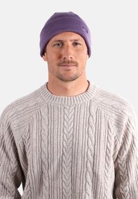 Un bonnet en tricot violet avec une texture côtelée, associé à un pull en maille légère gris clair présentant des motifs en relief et un col rond.