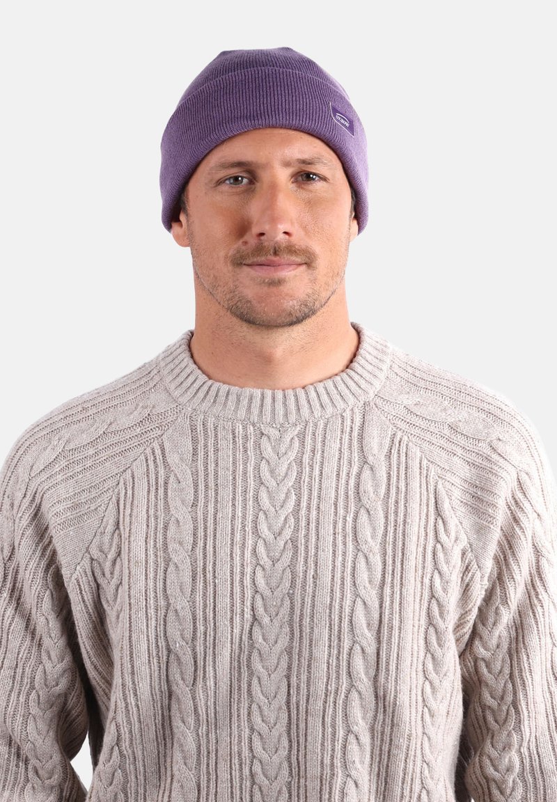 Un bonnet en tricot violet avec une texture côtelée, associé à un pull en maille légère gris clair présentant des motifs en relief et un col rond.