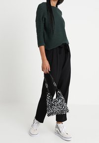 Top de manga larga verde con canalé combinado con pantalones negros de pierna ancha. Un bolso negro adornado con una correa estampada y zapatillas blancas.