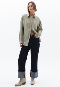 Camicia verde chiaro con bottone, dal taglio rilassato, abbinata a jeans cropped blu scuro con risvolti in denim e righe orizzontali, completata da stivaletti beige alla caviglia.