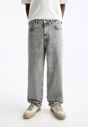 Lichtgrijze baggy jeans met een vervaagd textuur, vijf zakken en een knoopsluiting, gecombineerd met crèmekleurige en beige sneakers.