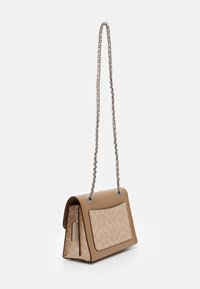 Beige olkalaukku, jossa on ketjusanka, joka on valmistettu sileästä nahasta ja jossa on kuviollinen etupinta, koristeltu metallikoristeilla ja niiteillä.