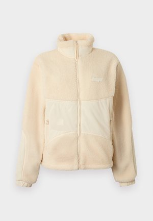Beige fleecejack met ritssluiting, opstaande kraag, twee voorzakken met rits, elastische manchetten en een klein logo op de linkerborst.