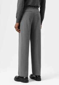 Pantalon gris à jambes larges en tissu texturé, doté de deux poches arrière, de passants pour ceinture, et porté avec des chaussures noires.