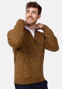 Brown, textured zip-up sweater with long sleeves and side pockets, featuring a subtle pattern and ribbed cuffs and hem.