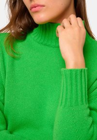 Pull en tricot vert avec un col haut et côtelé et un tissu texturé. Les manches présentent des poignets côtelés, offrant un ajustement parfait.