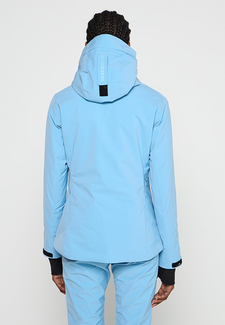 Jasnoniebieska wodoodporna kurtka o dopasowanym kroju, z regulowanym kapturem i czarnymi akcentami. Posiada teksturowany materiał oraz logo na plecach.