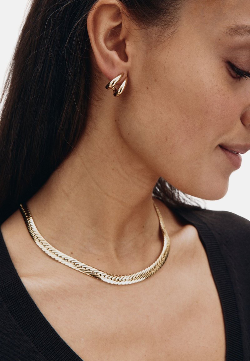 Kullatooni ehted sisaldavad lamedat, kett-link kaelakeed ja pisarakuju rõngakõrvarõngast. Sile, läikiv tekstuur keerukate detailidega.