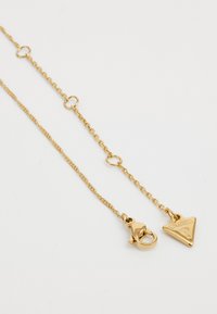 Gouden ketting met een driehoekige hanger met het geperste "GUESS" logo. Voorzien van een kreeftsluitingen en ronde schakels voor de verstelbare lengte.