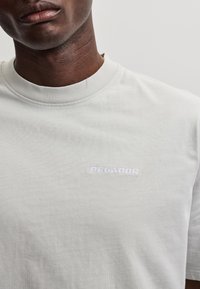 Άνδρας που φοράει απλό λευκό T-shirt με μικρό, λευκό κεντητό λογότυπο "PEGADOR" στο αριστερό στήθος.