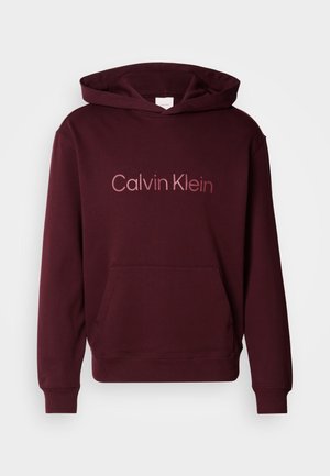 Bordový mikina s kapucňou a predným vreckom, na ktorom je svetlejším písmom logo "Calvin Klein". Vyrobená z mäkkej zmesi bavlny.