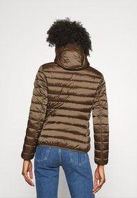 Bruine donzen jas met capuchon, met een doorgestikt ontwerp en een gladde, glanzende textuur. Draagt een blauwe spijkerbroek, die een casual look toont.