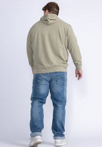 Felpa khaki con cappuccio e maniche lunghe, vestibilità rilassata. Abbinata a jeans in denim azzurro chiaro con tasche posteriori e orli risvoltati. Calzature casual visibili.