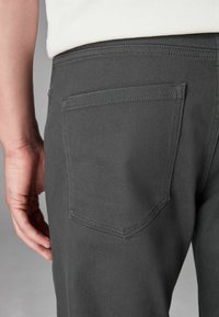 Pantaloni din denim de culoare gri închis, cu un singur buzunar posterior cu o formă subtilă și ascuțită, cusătură dublă și un finisaj neted, texturat.