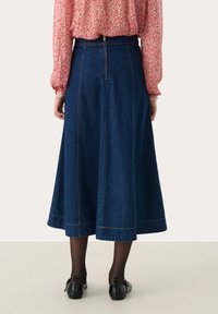 Denim midi sukně s volným střihem, tmavě modré barvy a viditelným švem. Obsahuje zapínání na zip v zadní části a rozšířený lem.