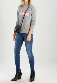 Šedá mikina s barevným textem, modré skinny džíny a černé kotníkové boty na podpatku. Stylový a přiléhavý design po celém oblečení.