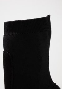 Calcetín negro con un upper texturizado, puño acanalado y cuerpo liso, diseñado para la comodidad y facilidad de uso.