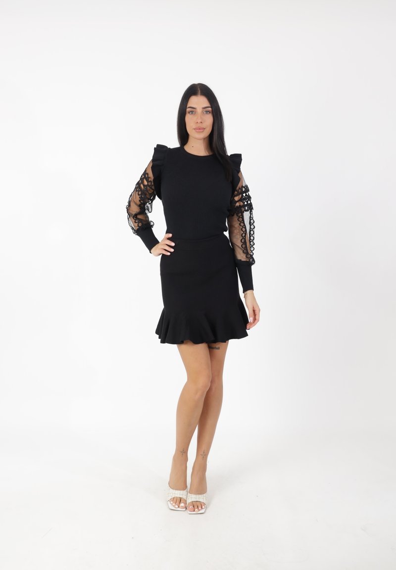 Vestido negro con cuerpo ajustado y dobladillo con volantes, con mangas transparentes y estampadas. Combinado con zapatos de tacón destalonados con tiras en el tobillo.