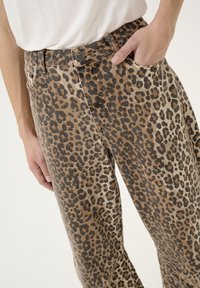 Pantalons en coton imprimé léopard avec taille haute, design classique à cinq poches et coupe décontractée, avec des coutures visibles et une fermeture à bouton.