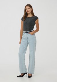 Top nero a maniche corte, jeans azzurri a vita alta con taglio dritto e décolleté nere a punta. Tessuto leggero nei jeans con delicate macchie.
