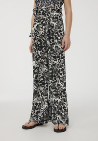 Pantaloni a gamba larga con motivo floreale in bianco e nero, con vita con cintura e tessuto leggero, abbinati a infradito nere.