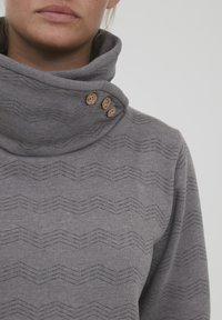 Šedá mikina s kapucí a texturovaným zigzag vzorem. Obsahuje tři dřevěné knoflíky na krku a má měkkou, hladkou texturu látky.