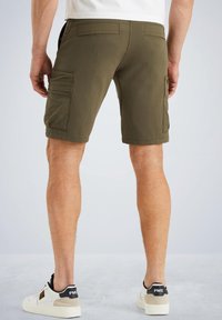 Shorts vert olive avec deux poches cargo sur les côtés, texture lisse et design ajusté. Portés avec des baskets blanches avec des accents noirs.