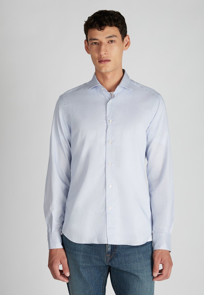 Lichtblauw gestreepte lange mouw shirt met een button-down kraag en witte knopen, gecombineerd met blauwe spijkerbroek. Glad textuur van de stof.