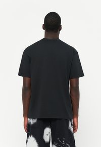 Svart bomull t-shirt med rund halsringning och korta ärmar, visad bakifrån. Materialet verkar slätt med en avslappnad passform.