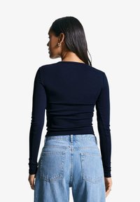 Navy long-sleeve top with a fitted design, paired with light blue high-waisted jeans featuring two back pockets and a relaxed fit.