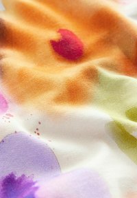 Tissu doux avec des motifs abstraits colorés en aquarelle dans des tons orange, rouge, violet et vert, présentant des plis doux et une texture.