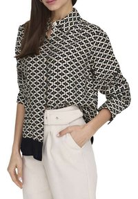 Chemise à boutons à motifs noir et blanc avec un col, des manches longues et une coupe légèrement courte ; associée à un pantalon taille haute de couleur claire.