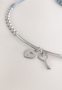Silbernes Armband mit runden Perlen und zwei herzförmigen Anhängern, einer mit einem Schloss und einer in Form eines Schlüssels mit Herz-Ausschnitt.