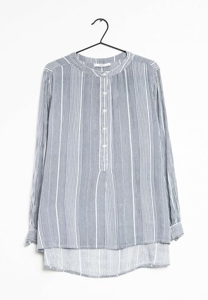 Chemise à manches longues boutonnée avec des rayures verticales blanches et noires, col rond, suspendue sur un cintre noir sur fond blanc.